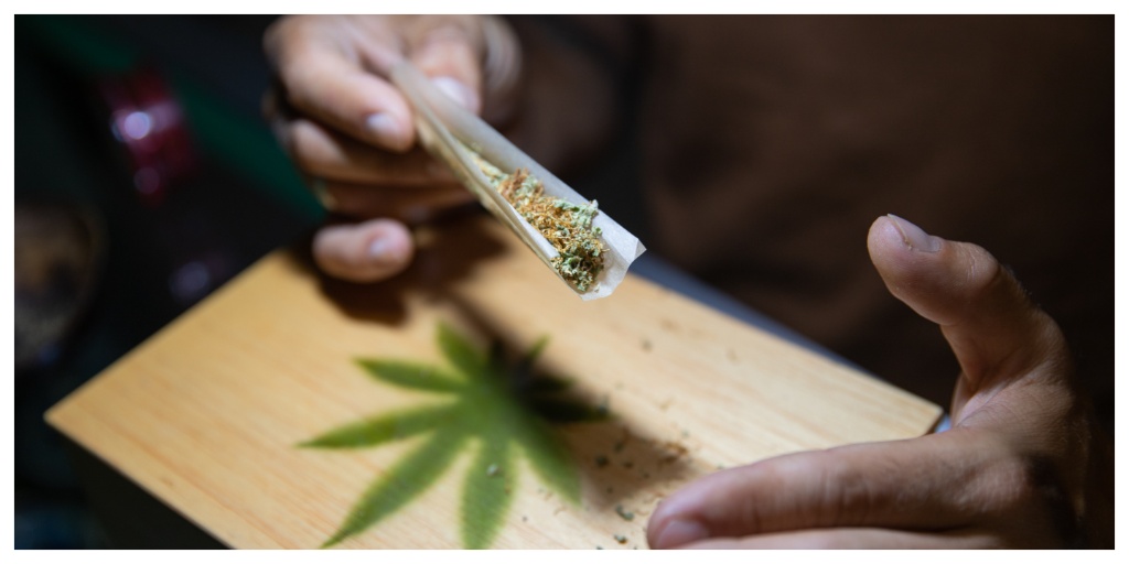 Close-up of the hands of a boy who is rolling a joint of marijuana. Focus on the marijuana