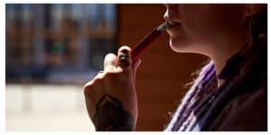 Close-up of young woman with tattoo on hand holding electronic vape