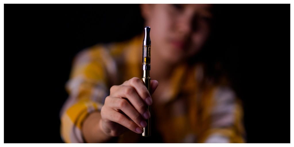 Teenage girl vaporize cannabis through a vaporizer containing cannabis oil in a tube after electrical heating