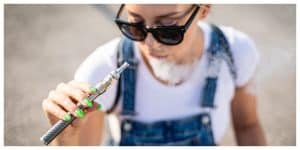 Modern woman outdoor smoking weed pen while sitting at city street