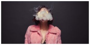 girl in pink fur coat exhaling smoke, grey background