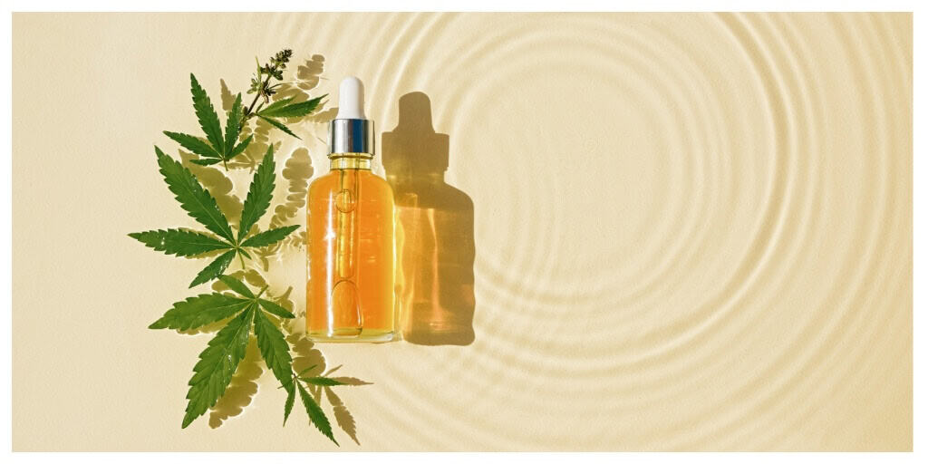 bottle with cbd oil floating on water above a beige surface. cannabis leaves floating next to the bottle, waves on the surface