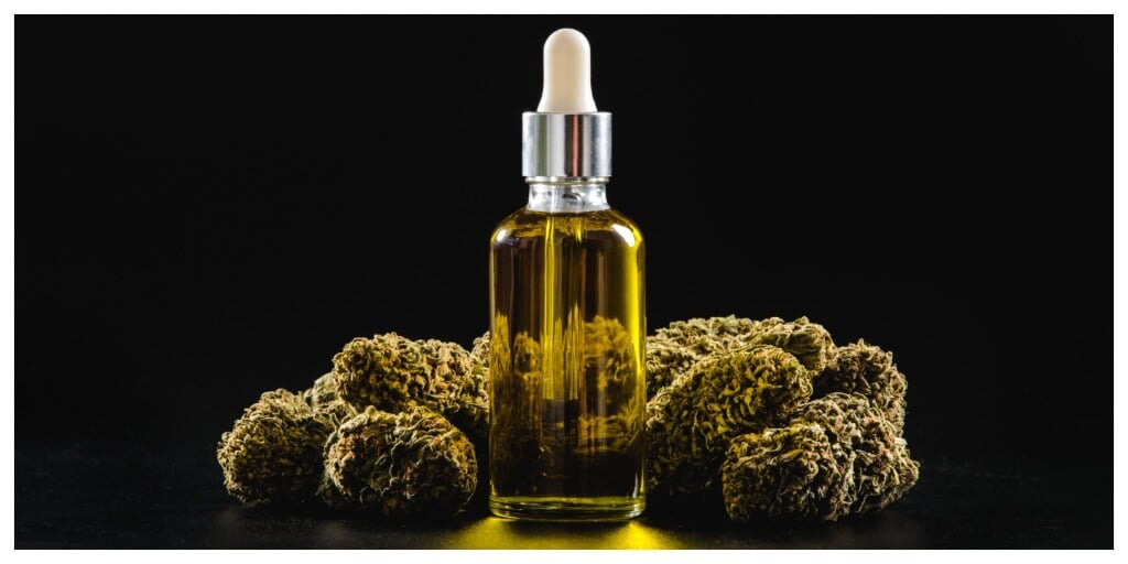 Marijuana buds with a bottle of CBD oil extract with a dark background