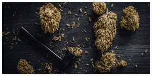 Dry cannabis buds with metal smoking pipe on a black table